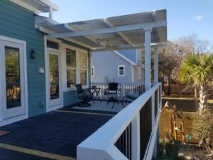 A backyard porch with a dark deck, white railings, and a patio cover
